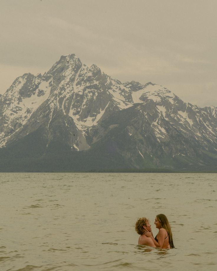 two women are in the water with mountains in the backgrouds and one is holding her head