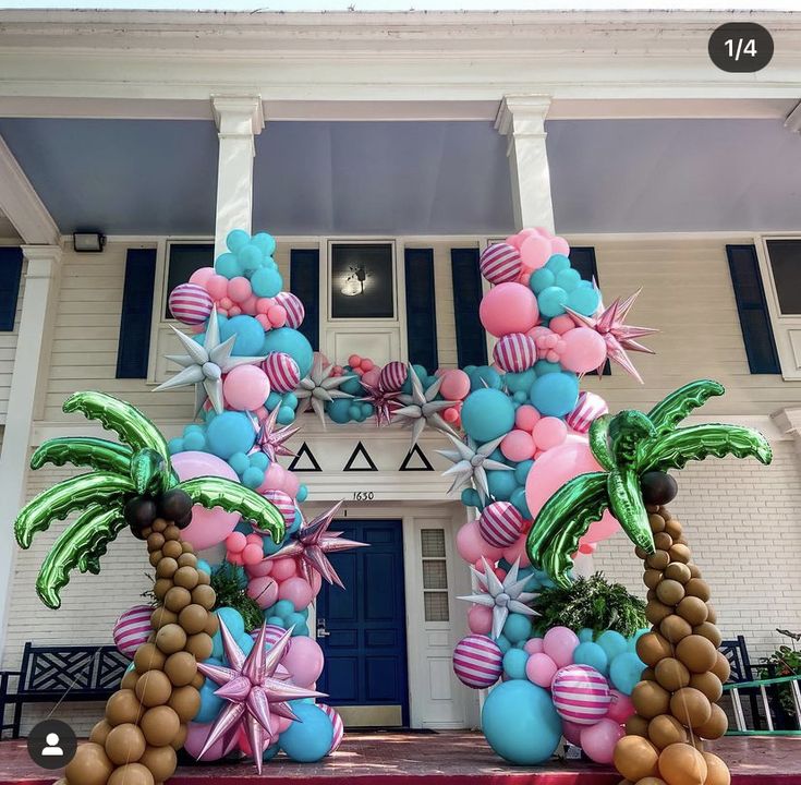 a large balloon arch decorated with palm trees and beach balls in front of a white building