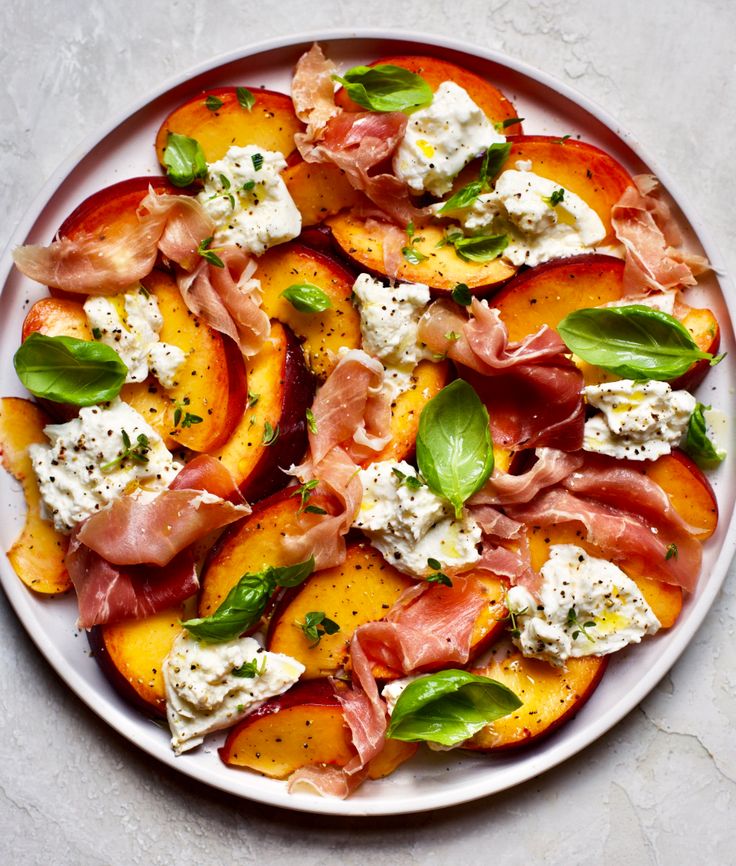 a white plate topped with peaches covered in prosciutto and basil leaves