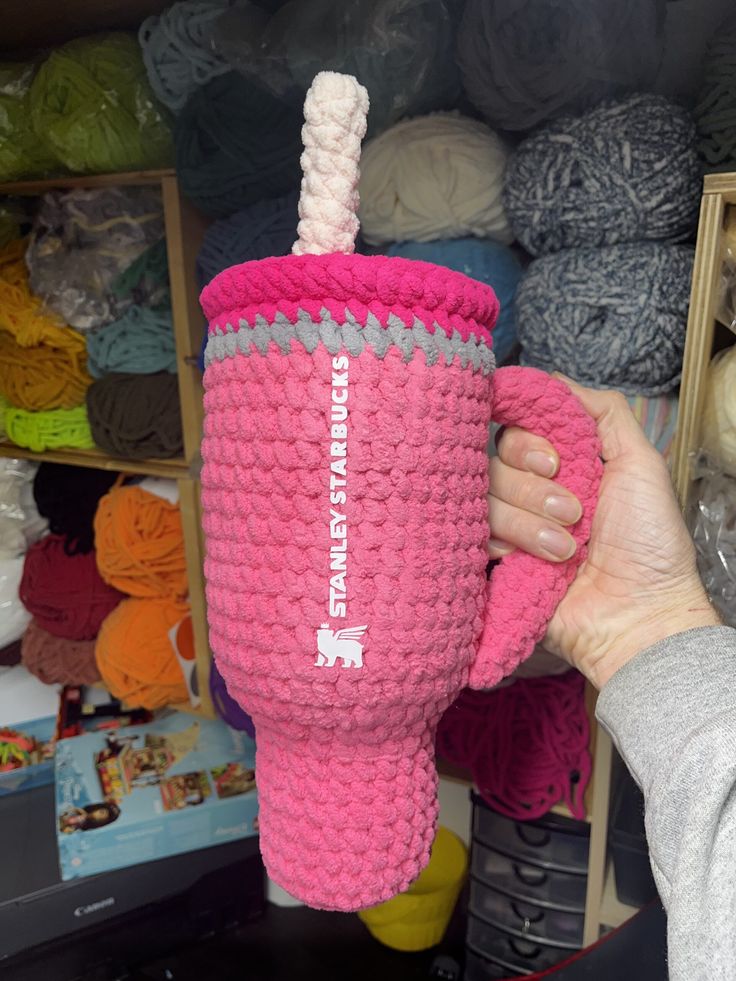 a person holding up a pink cup with a straw in it and yarn balls behind it