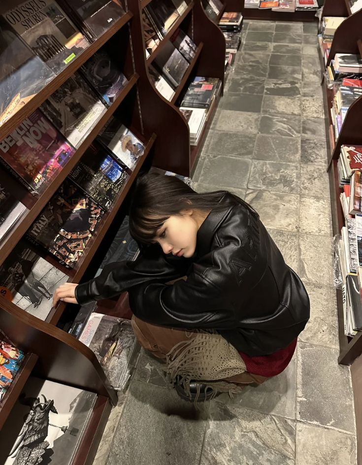 a woman sitting on the ground in front of a bookshelf filled with magazines