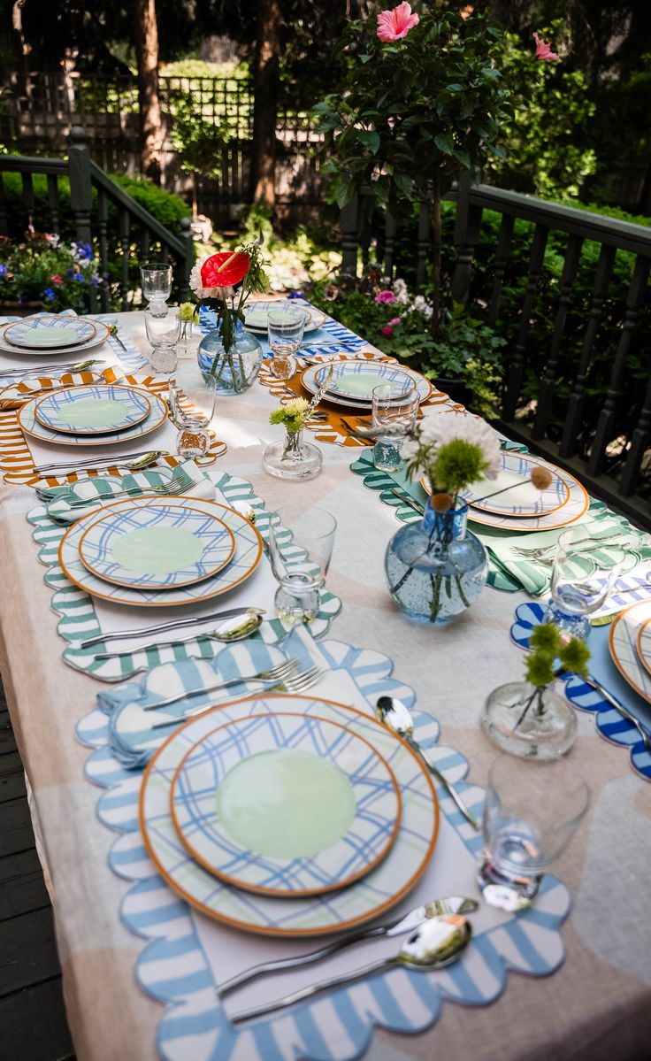 a long table with plates and flowers on it is set for an outdoor dinner party