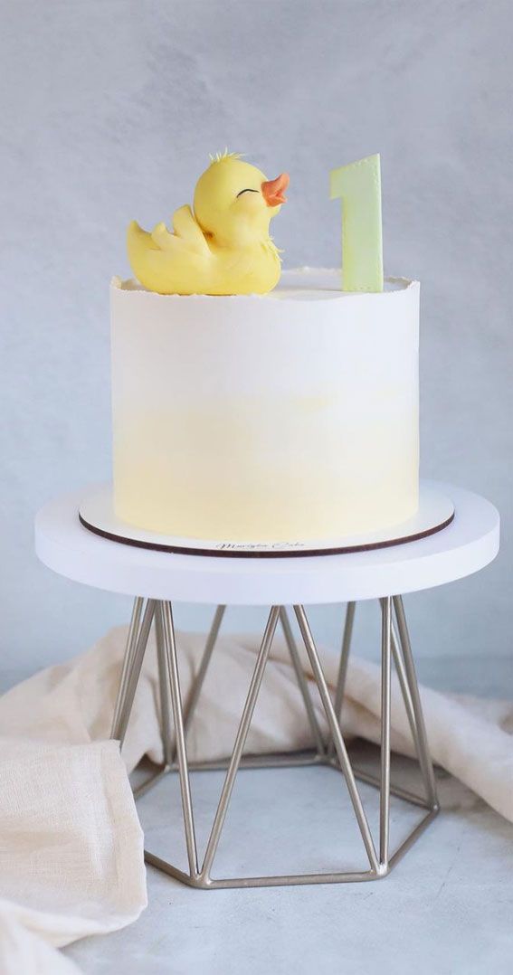 a white cake with a yellow rubber ducky in the middle on a metal stand