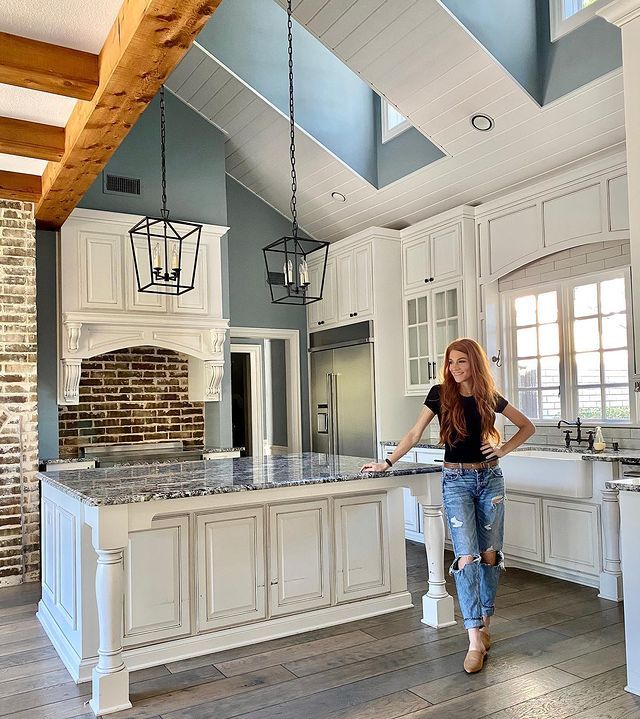 a woman standing in the middle of a kitchen with an island counter top and white cabinets