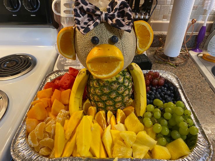 a metal tray filled with fruit and a stuffed animal wearing a bow on it's head