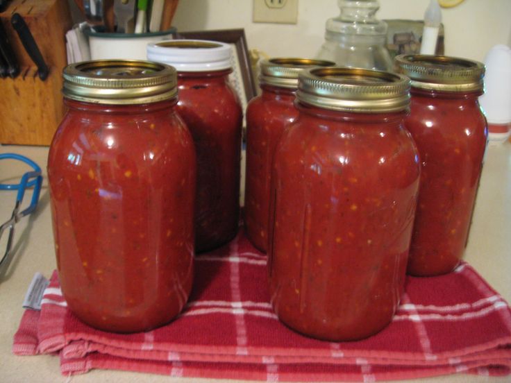 three jars filled with red sauce sitting on top of a table next to a pair of glasses