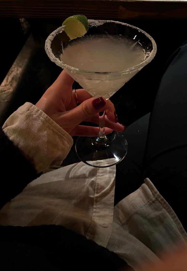 a person holding a martini glass with a lime on the rim in front of them