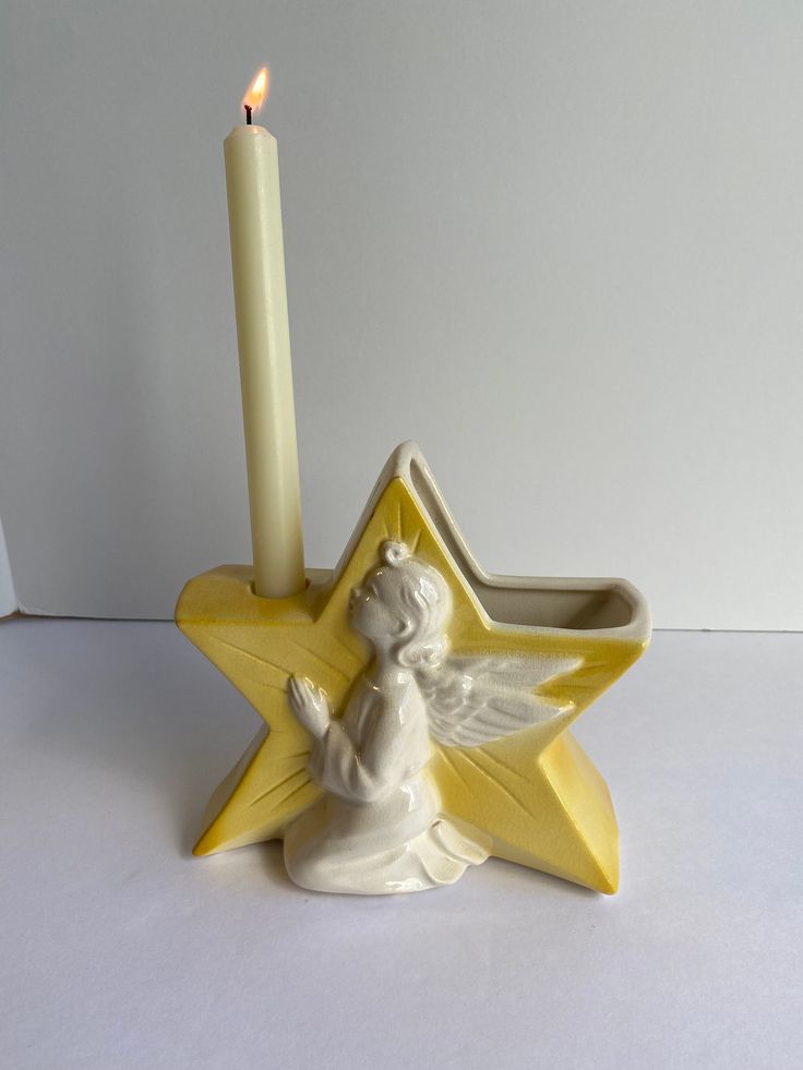 an angel candle holder with a lit candle in the middle and a star on top