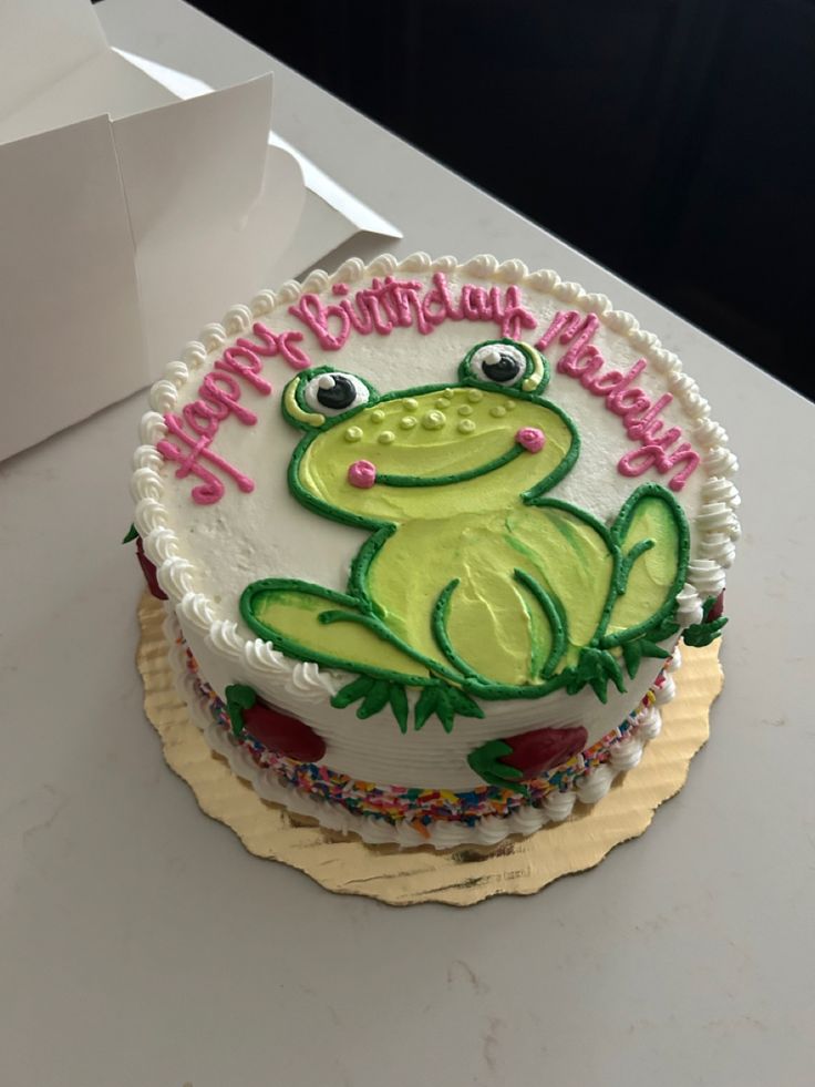 a birthday cake with a frog design on it sitting on a table next to a box