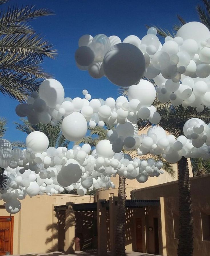 white balloons are floating in the air near palm trees