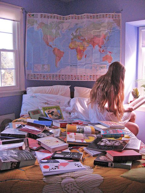 a woman sitting on top of a bed with lots of books in front of her