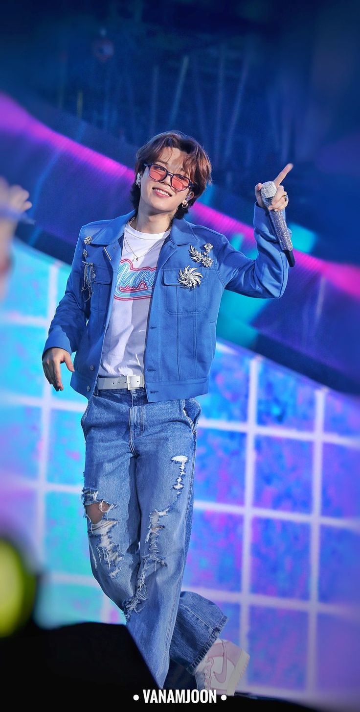 a male in a blue jean jacket and white t - shirt is dancing on stage