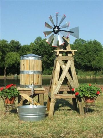 an old fashioned windmill sits in the middle of a field with potted plants and buckets