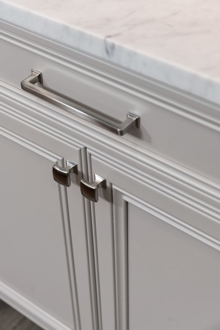 an image of a kitchen cabinet with marble top and stainless steel handle pulls on it