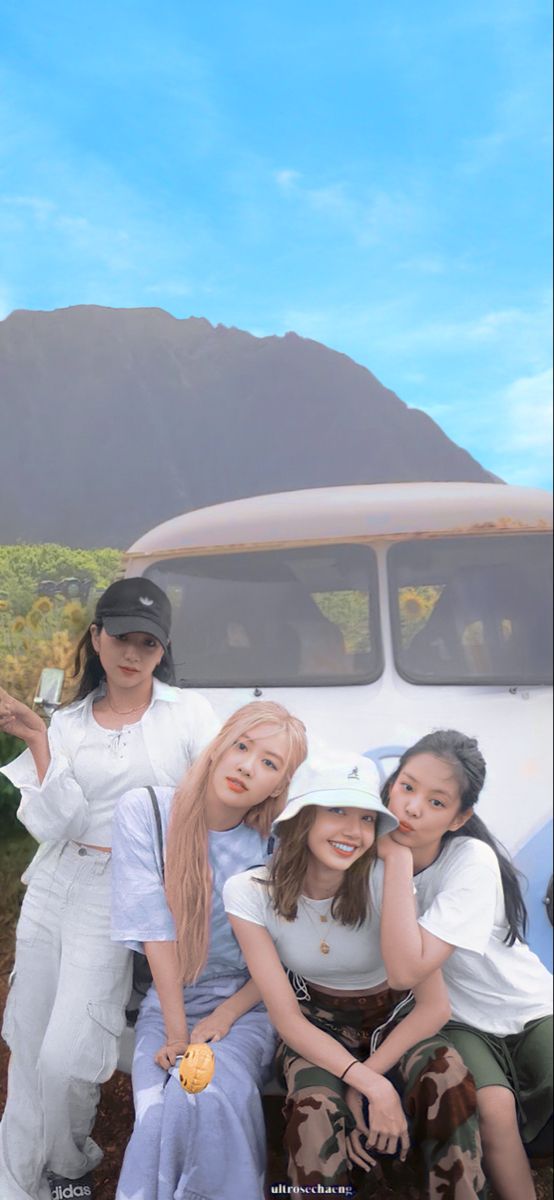 four girls are posing in front of an old car with mountains in the back ground