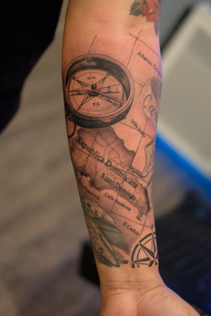 a person with a tattoo on their arm holding up a compass and other things in the background