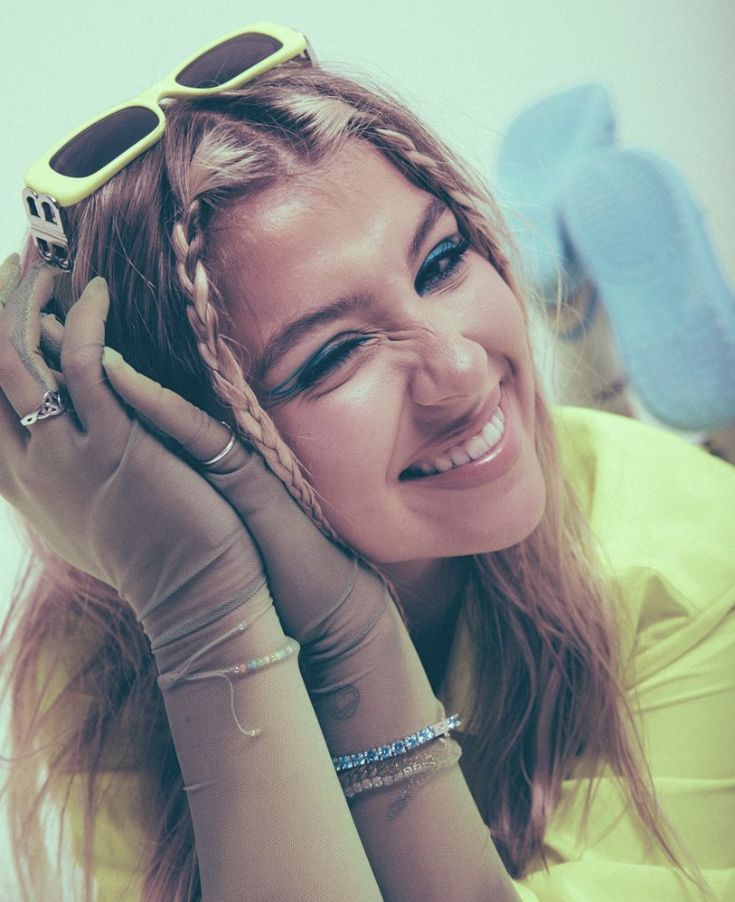 a woman in yellow shirt and gloves holding her hands up to her face while smiling