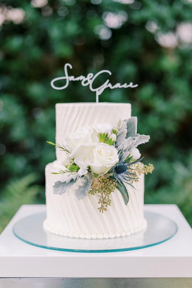 a wedding cake with white flowers and greenery on top is sitting on a table