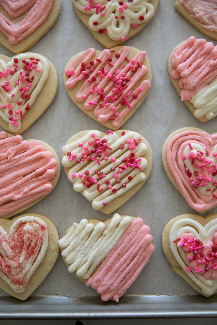 heart shaped cookies with pink icing and sprinkles on a baking sheet