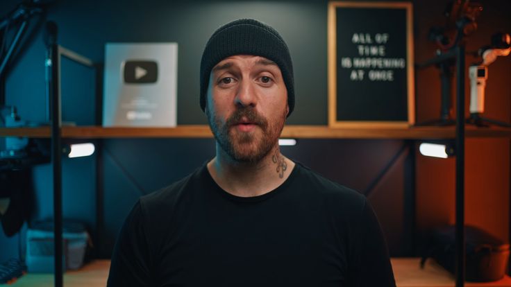 a man wearing a beanie standing in front of a desk with microphones on it