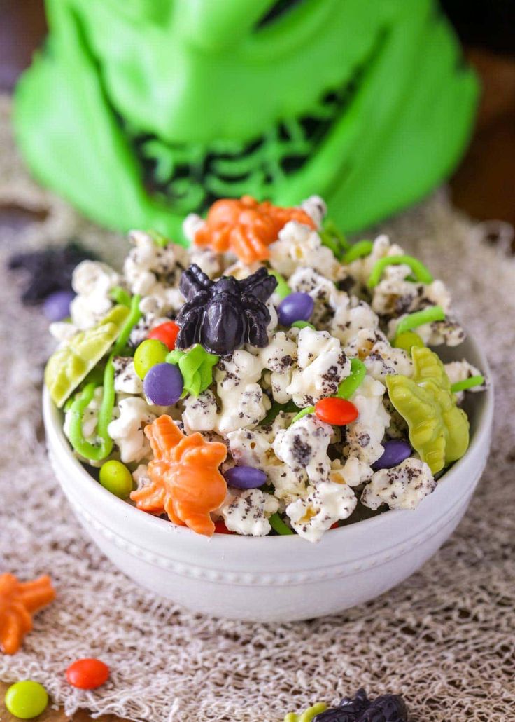 a white bowl filled with halloween popcorn on top of a table next to candy candies