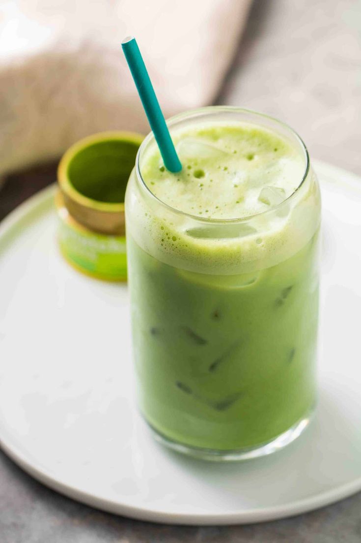 a green smoothie on a white plate with a blue straw in the middle and two small cups behind it