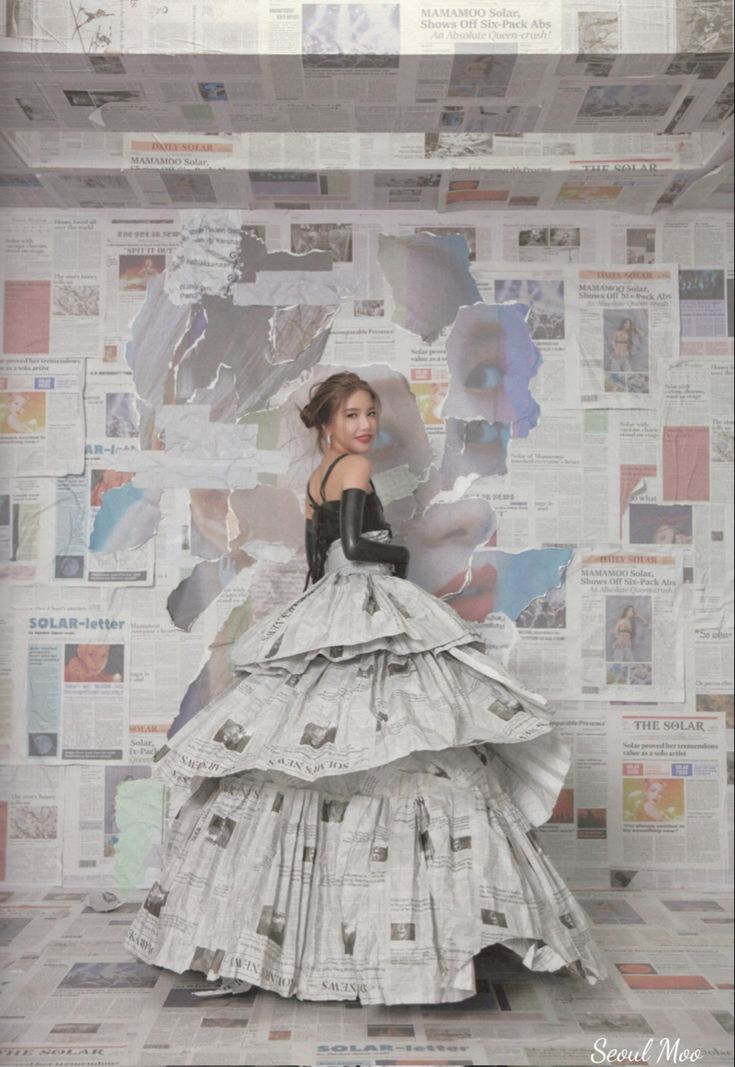 a woman in a dress made out of newspaper paper is standing against a wall full of newspapers