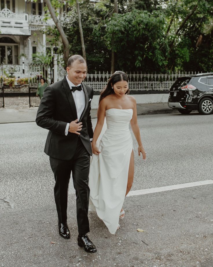 a bride and groom walking down the street in their tuxedo attire, holding hands