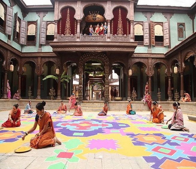 several people sitting on the ground in front of a building with colorful carpet covering it