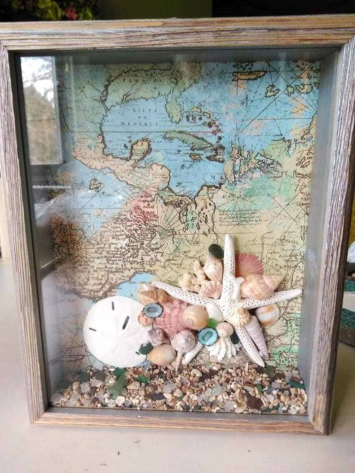 shells and seashells are placed in a shadow box on a table next to a map