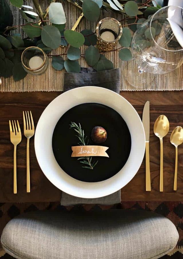 a black soup in a white bowl on top of a table with gold utensils