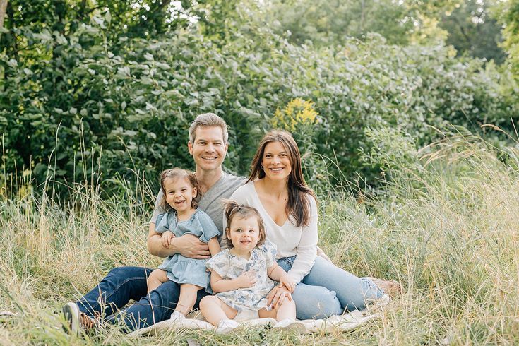 a man and woman sit on a blanket with their two children in a field full of tall grass