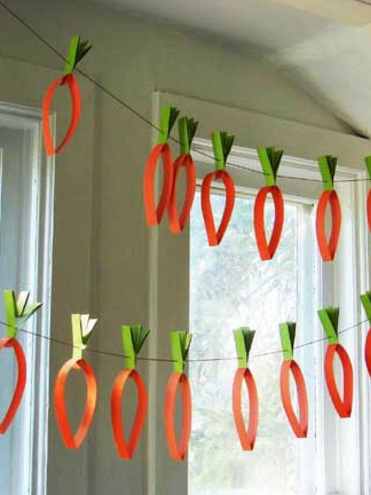 some paper carrots are hanging from a line in front of a window with white curtains