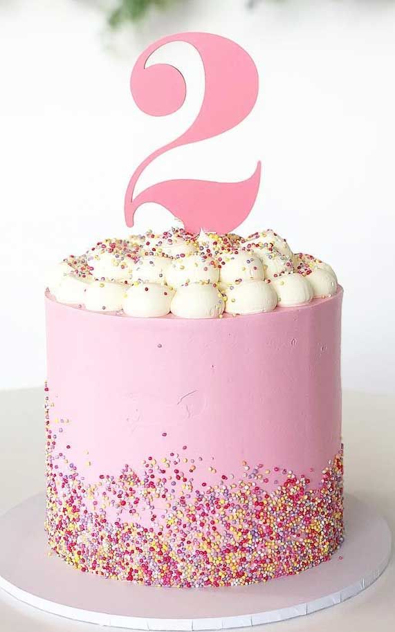 a birthday cake with sprinkles and a pink number two topper on it