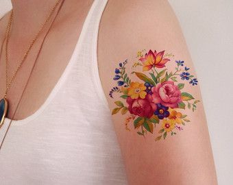 a woman with a flower tattoo on her left arm and right arm is wearing a white tank top