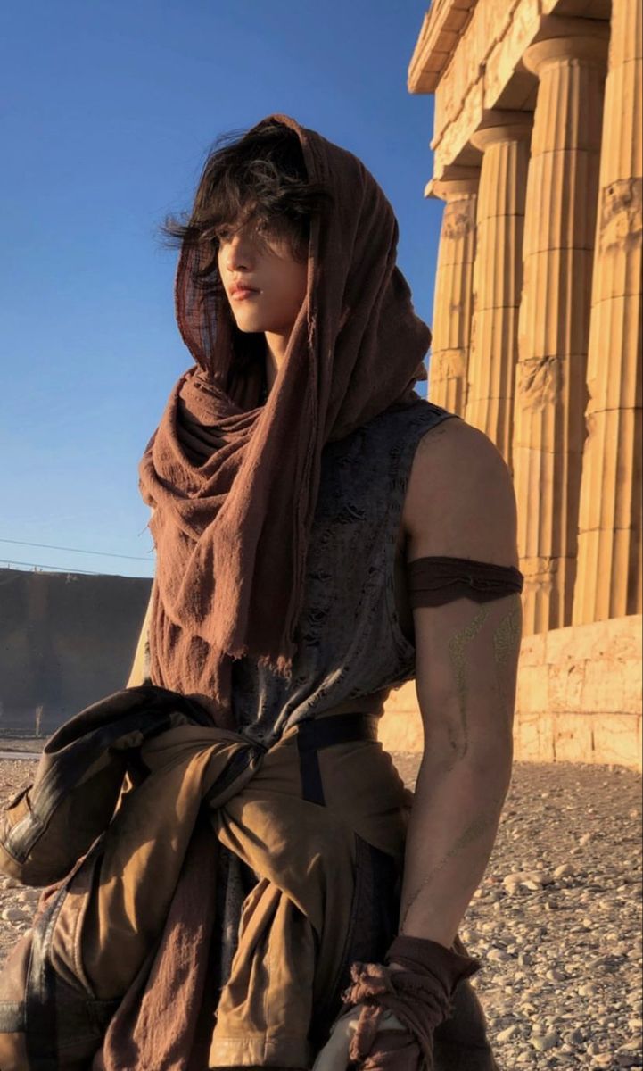 a man with a scarf on standing in front of an ancient building