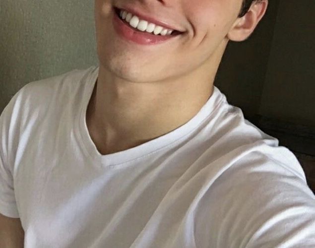 a smiling young man wearing a white t - shirt