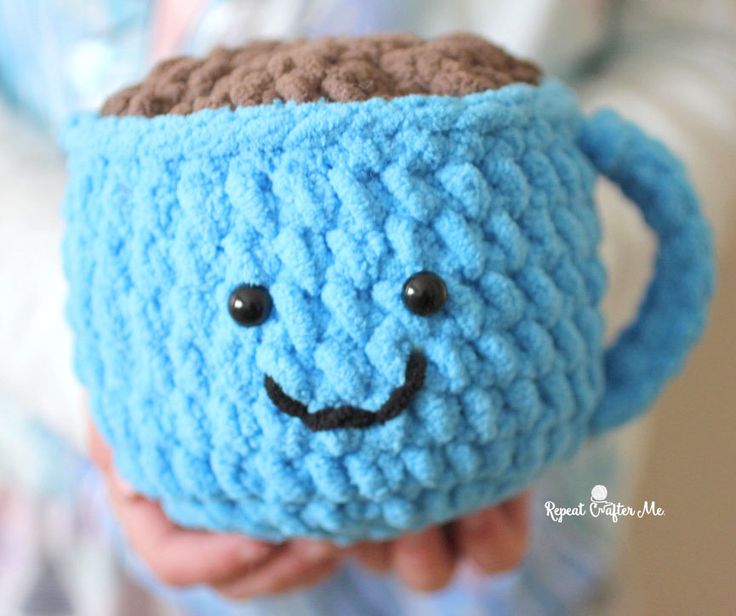 a crocheted blue coffee cup with a smiling face on it's side