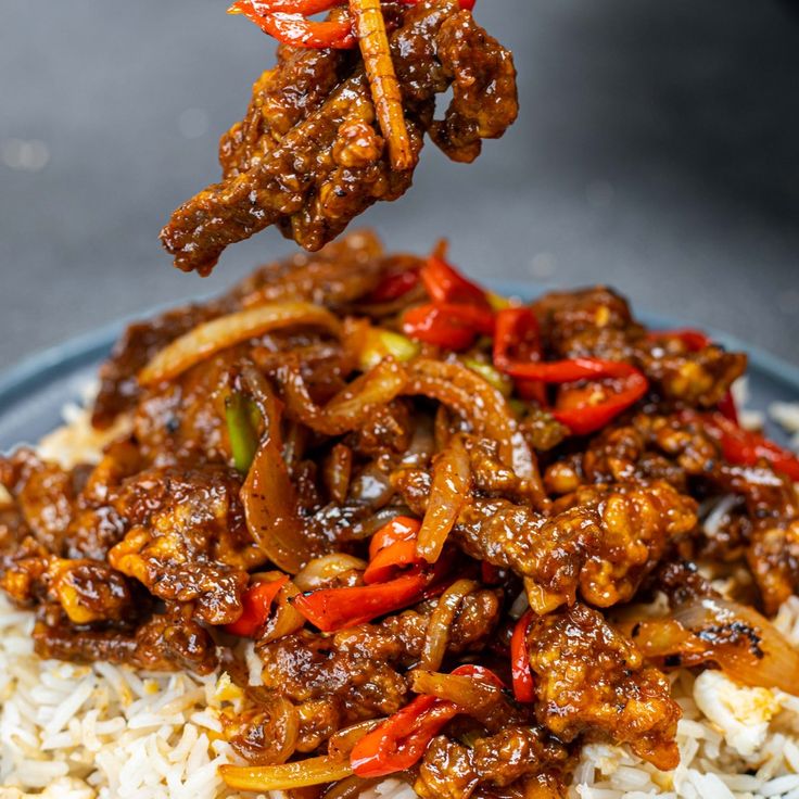 a blue plate topped with rice and meat next to chopsticks sticking out of it