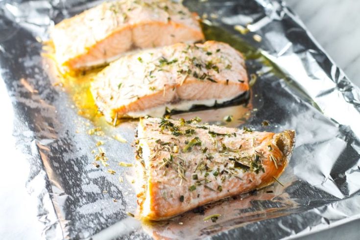 three salmon fillets sitting on top of aluminum foil covered in seasoning and herbs