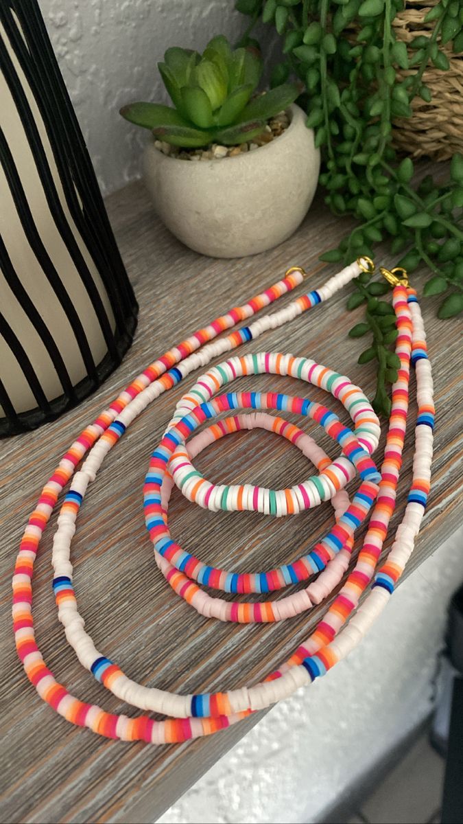 multicolored beaded necklaces sitting on a table next to a potted plant