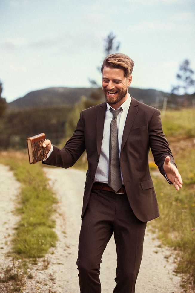 a man in a suit and tie walking down a dirt road holding an open book