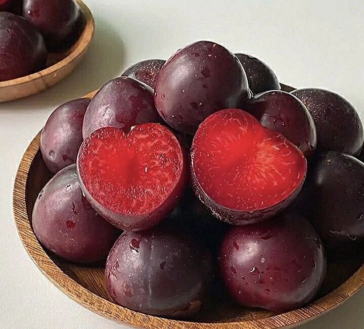 a wooden bowl filled with purple plums on top of a white table next to another bowl