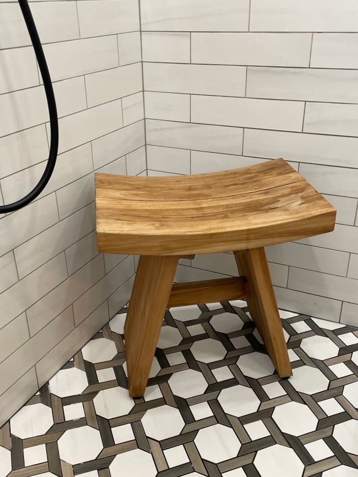 a wooden stool sitting on top of a tiled floor next to a shower head and hose