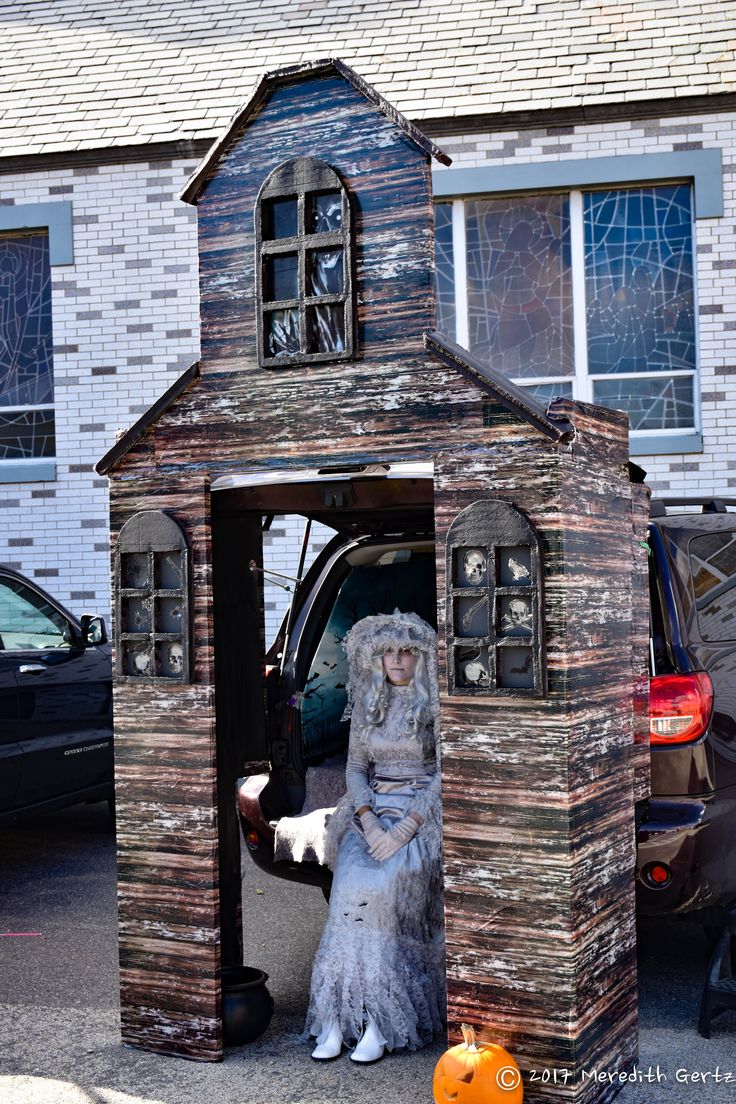 a woman sitting in the back of a small wooden structure next to a black car