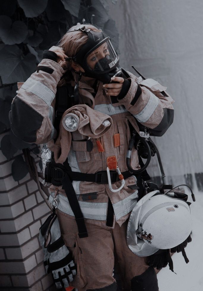 a fireman in full gear standing next to a brick wall and holding a helmet