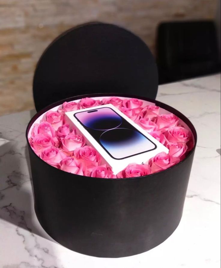 a black box with pink roses in it and a cell phone on the lid, sitting on a table