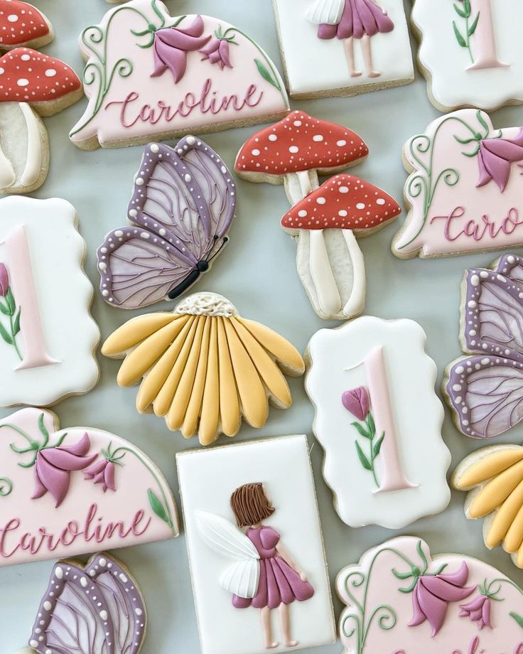 decorated cookies are arranged in the shape of flowers, mushrooms, and fairy wings for a first birthday party