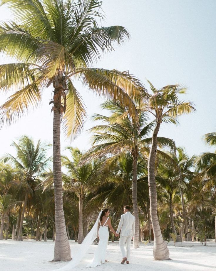 a bride and groom walking under palm trees