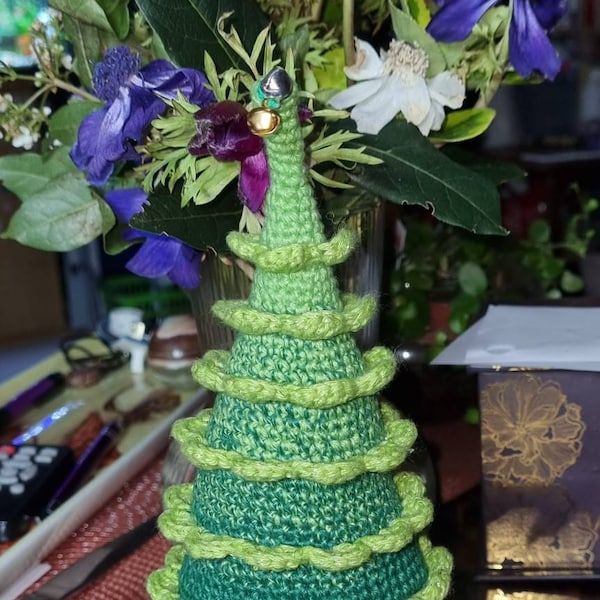 a crocheted christmas tree sitting on top of a table next to purple flowers